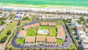 Luftaufnahme eines Hotels an der Küste mit einem zentralen Pool, umgeben von Parkplätzen und direktem Zugang zum Strand.