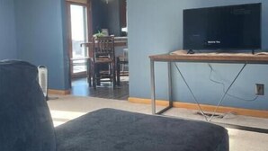 A living room with a dark blue couch, a flat-screen TV on a wooden stand, and a dining area in the background. - LaCreek Lodge-5 beds (Martin)