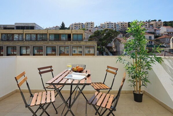 Une terrasse sur le toit, avec une table et des chaises en bois, un pot de fleurs et une vue sur les immeubles d’habitation en arrière-plan.