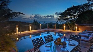 Un espace extérieur avec une piscine, une table et des chaises, le tout entouré d’une clôture et de palmiers.
