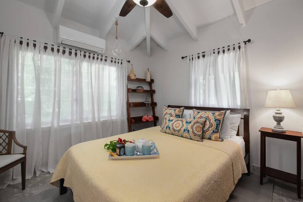 A bedroom with a bed, bedside table, lamp, and a tray with items on the bed.