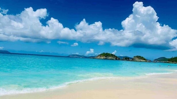 A beach with clear turquoise water, white sand, and small green islands in the distance.