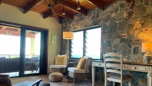 A cozy room with a stone wall, a wooden ceiling, a desk with a lamp, and comfortable seating.