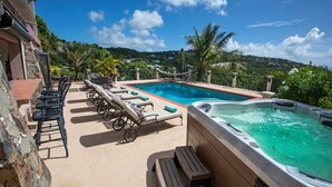 A rooftop pool area with lounge chairs, a hot tub, and a view of the surrounding landscape.