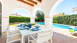 En udendørs terrasse med et spisebord, en pool og udsigt over den omkringliggende have.