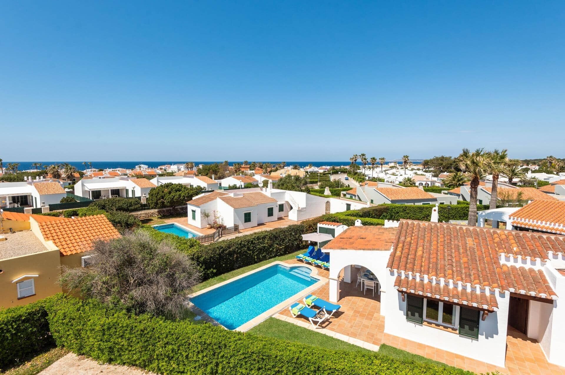 A coastal residential area with white houses, a swimming pool, and a view of the sea.