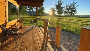 Une terrasse en bois offrant une vue sur un champ verdoyant et des arbres, le tout sous un ciel dégagé.