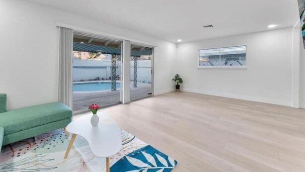 Un salon moderne avec un canapé vert, une table basse blanche et une vue sur une piscine, visible à travers des portes vitrées.