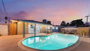 Une piscine dotée d’un patio couvert, entourée d’une clôture et bordée d’un bâtiment dont le toit est en pente.