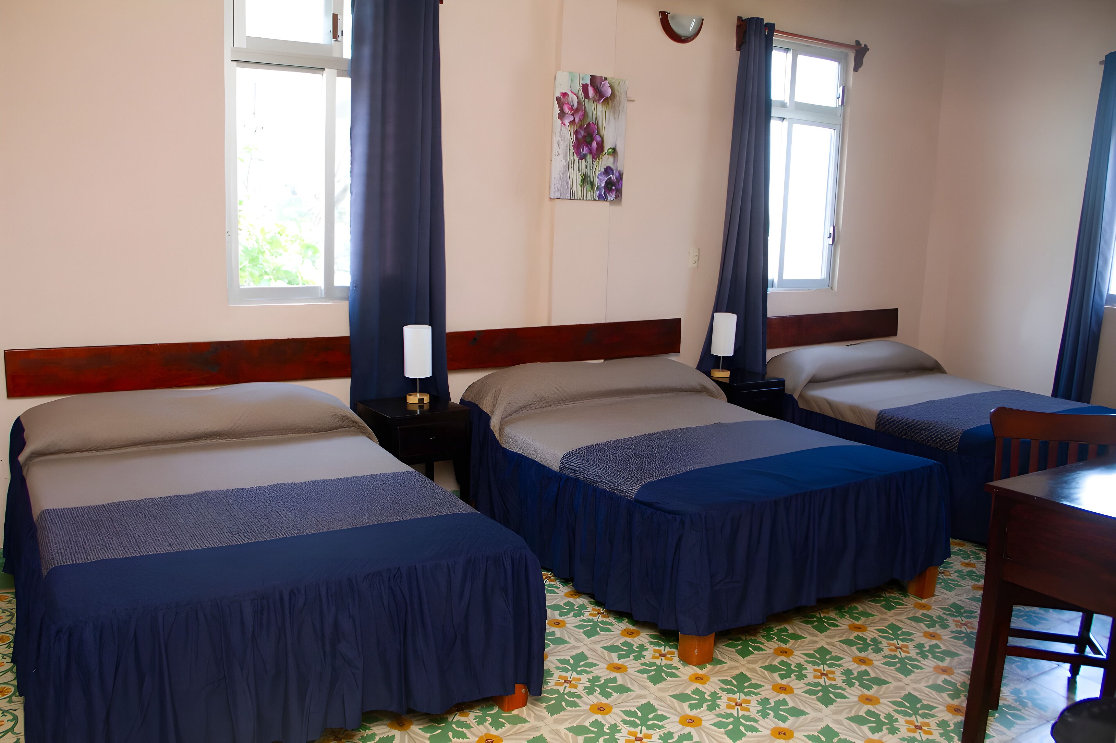 Ein Zimmer mit drei Einzelbetten, einem Holz-Kopfstück, einem kleinen Tisch und einer Wandleuchte.