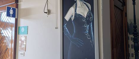 Paredes com um retrato emoldurado, um ventilador de teto, uma porta com olho mágico e uma pequena mesa com um vaso e revistas.