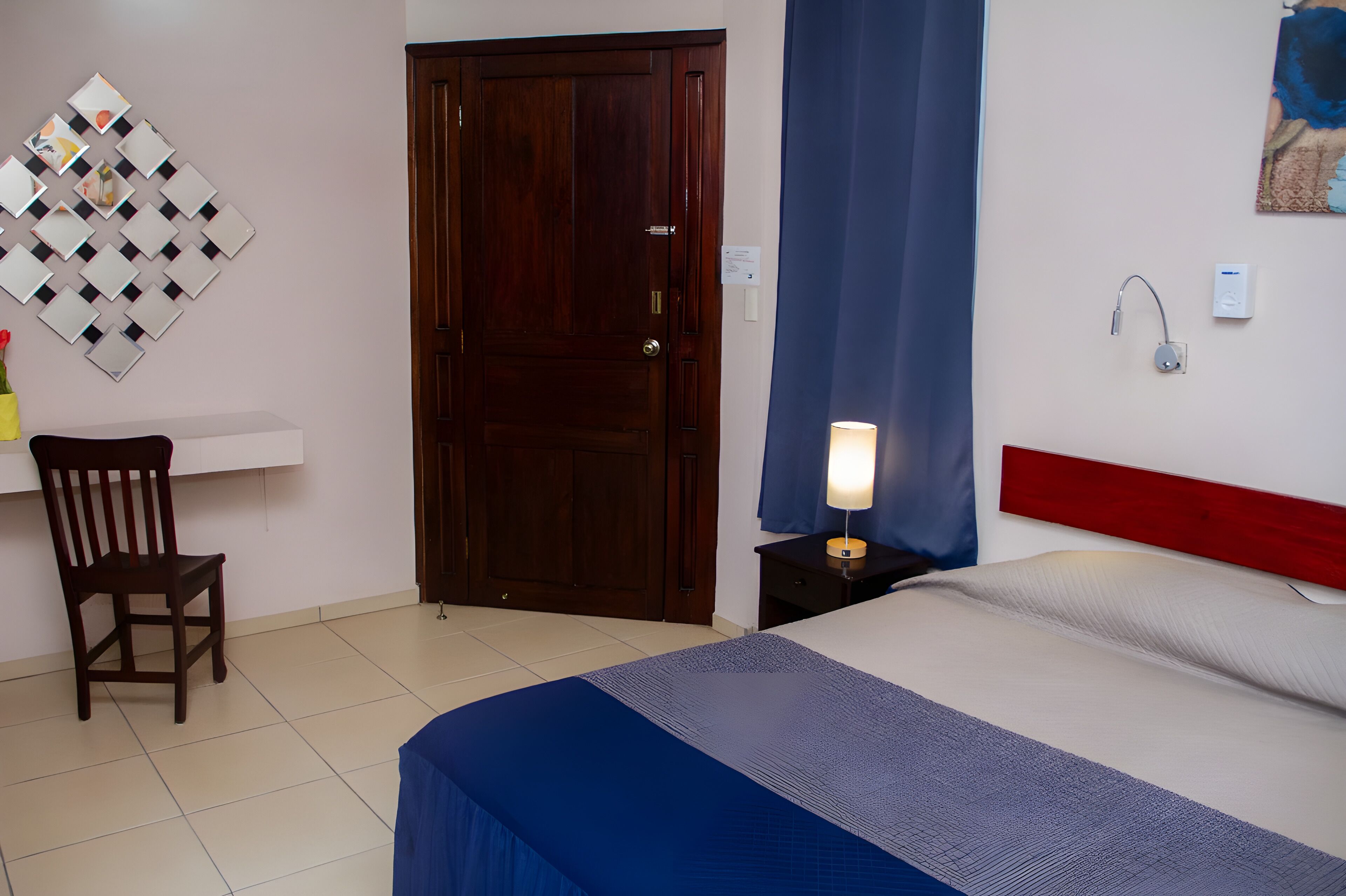 Ein Hotelzimmer mit Bett, Schreibtisch, Stuhl, Tür, Wandleuchte und Wandbild.