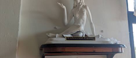 Escultura de una figura reclinada sobre una base de madera con una placa que dice 'Colección Eguan 2018'.