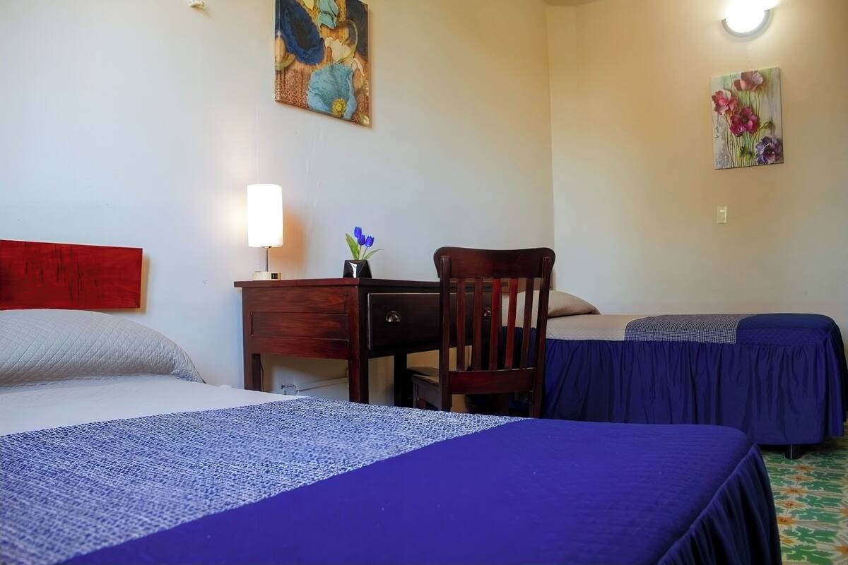 Ein Hotelzimmer mit zwei Betten, einem Schreibtisch mit Lampe, einem Sessel und Bildern an den Wänden.