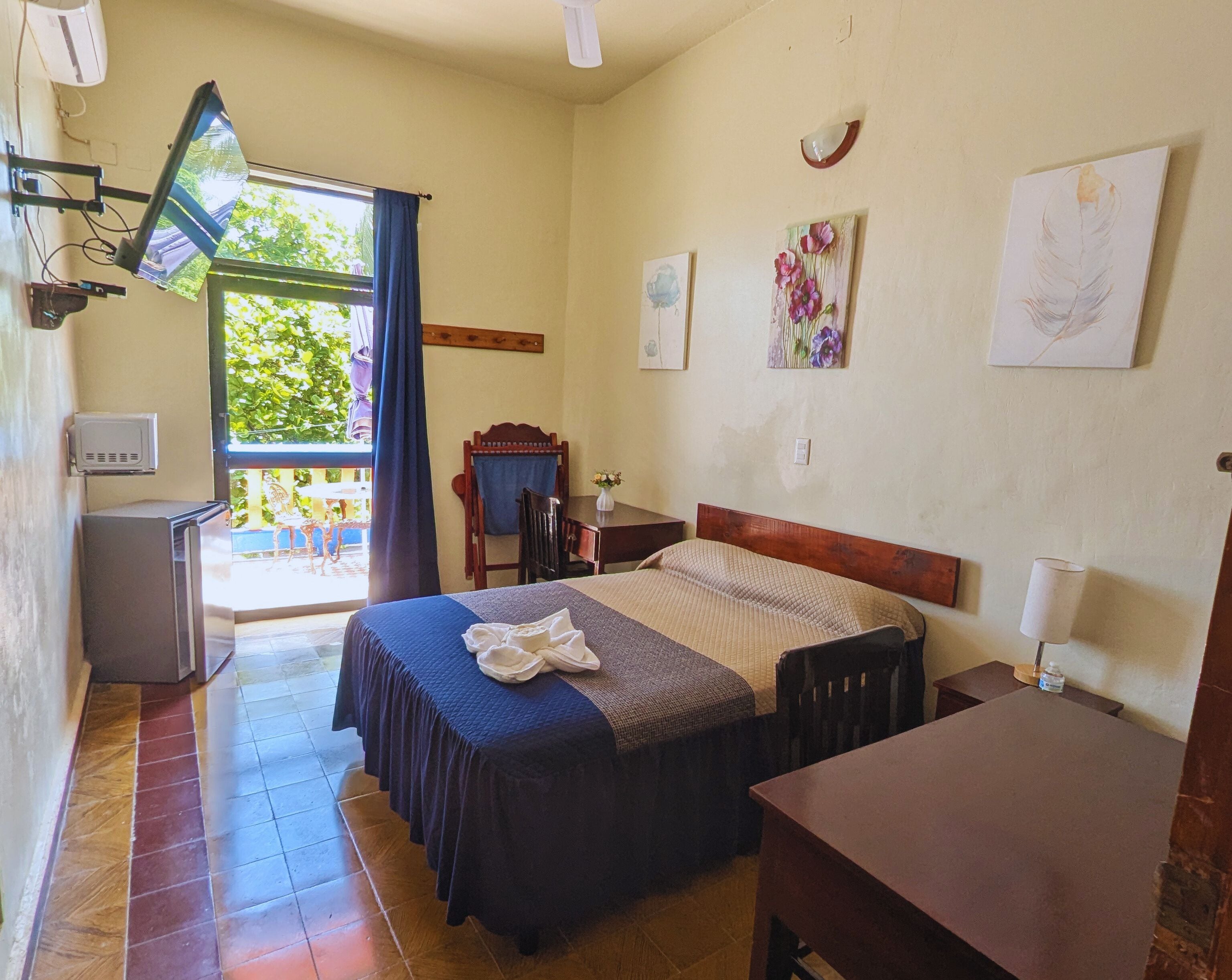 Una habitación con cama, escritorio, silla, televisión y un refrigerador pequeño.