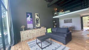 Un salon moderne avec un canapé gris foncé, un plancher en bois et un coin repas comprenant une table et des chaises.