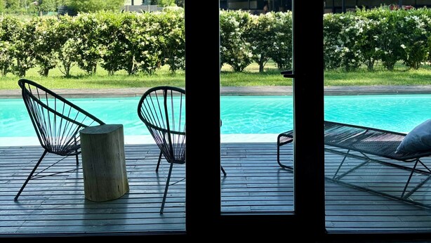 Un espace piscine avec des chaises et une terrasse en bois, donnant sur un jardin et un bâtiment.