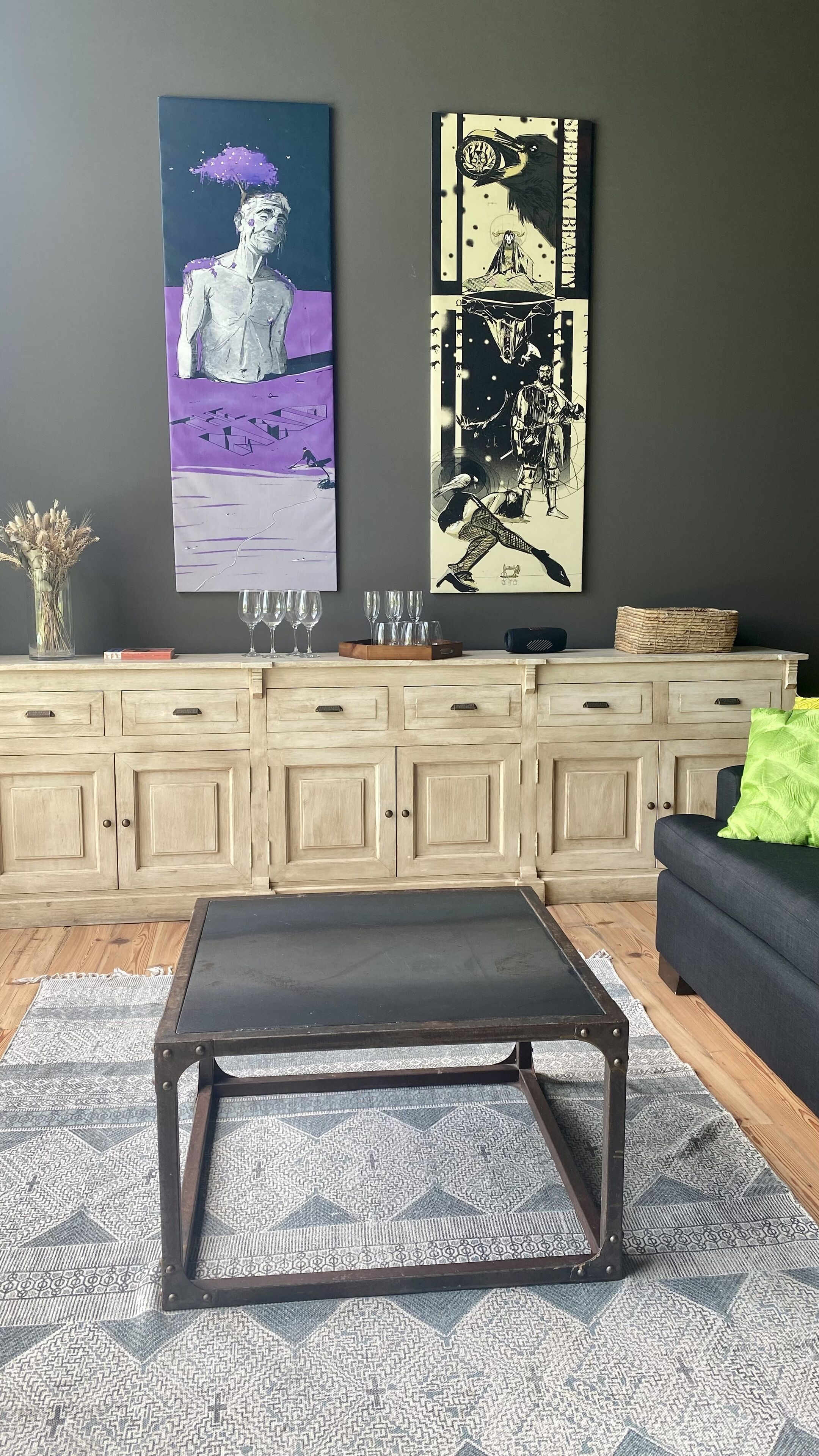 Un salón con pared gris oscura, un mueble de madera, un sofá negro y una alfombra estampada.