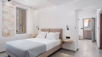 A modern bedroom with a large bed, bedside tables, a window with curtains, and a hallway leading to another room.