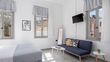 A modern room with a bed, a sofa, a small table, and two windows with curtains.