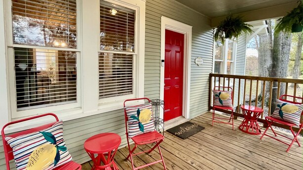 A porch with red metal chairs and a small table, a red door, and a welcome mat.