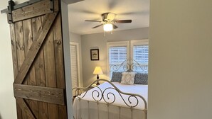 A bedroom with a bed, a ceiling fan, a window with blinds, and a wooden door.