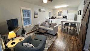 A compact living space with a sofa, a coffee table, a TV, and a dining area with stools.