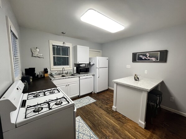 A compact kitchen with white cabinets, a gas stove, a microwave, and a refrigerator.