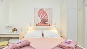 A hotel room with a bed, two pillows, a nightstand with a lamp, a vase with flowers, and a painting on the wall. - 5 Double room Villa Kate Dadić (Dubrovnik)