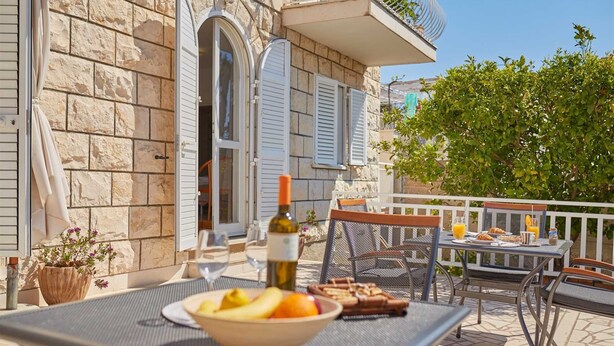 An outdoor dining area with a table set for two, a bowl of fruit, and a bottle of wine. - 6 Double Room in Villa Kate Dadić (Dubrovnik)