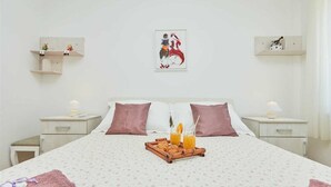 A neatly made bed with a tray of orange juice and a basket, two bedside tables with lamps, and wall shelves with decorative items. - 7 Double room with private external bathroom in Villa Kate Dadić (Dubrovnik)