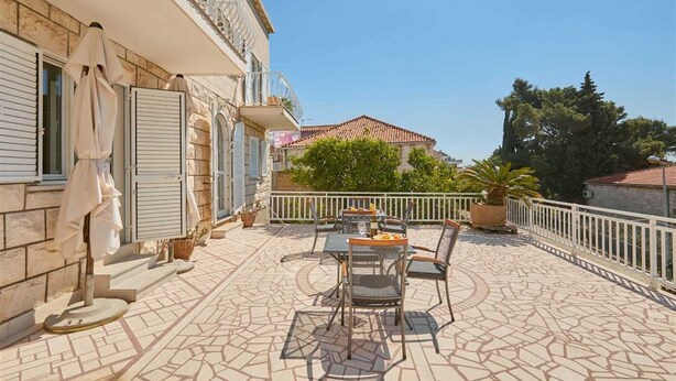 A terrace with a table and chairs, a potted plant, and a building with stone walls and shutters. - 7 Double room with private external bathroom in Villa Kate Dadić (Dubrovnik)