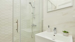 Une salle de bain moderne avec une douche en verre, un lavabo blanc et une petite plante en pot.