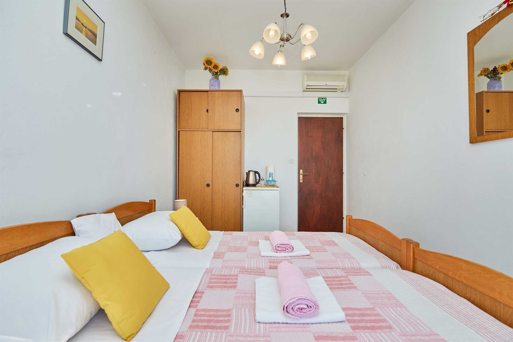 A hotel room with a bed, a wardrobe, a desk with a kettle, and a mirror.