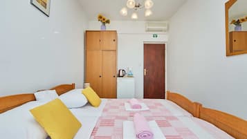A hotel room with a bed, a wardrobe, a desk with a kettle, and a mirror.