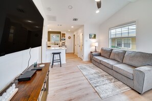 A modern living room with a flat-screen TV, a wooden coffee table, a grey sofa, and a patterned rug.