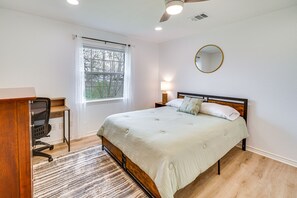 A bedroom with a bed, a desk, a chair, a window, and a ceiling fan.
