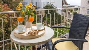 Een balkon met een tafel gedekt voor ontbijt, inclusief twee glazen jus d'orange, een beker en een bord eten.