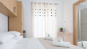 Een moderne hotelkamer met een groot bed, een houten kledingkast, een klein plankje met een plant en een douche.