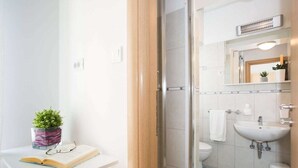 Een moderne badkamer met een douche, toilet en wastafel. Er is een klein plankje met een plant en een boek.