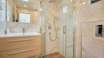 Un baño moderno con ducha de vidrio, tocador con azulejos de mármol y un espejo grande.