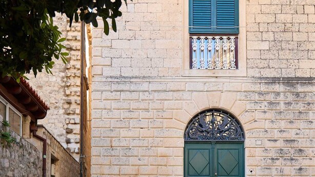 A stone building with a green door and blue shutters, a cobblestone street, and a tree in the foreground. - Dominium Premium Location Suites Duplex apartment 1 (Dubrovnik)