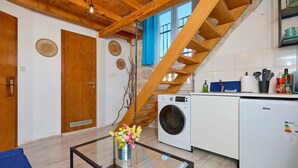 Cocina compacta con lavadora, refrigerador y zona de comedor con mesa de vidrio y sofá azul.