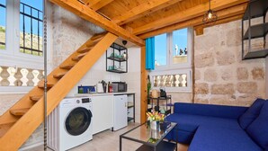 Un espacio habitable compacto con una escalera de madera, lavadora, sofá y una mesa de centro de cristal.