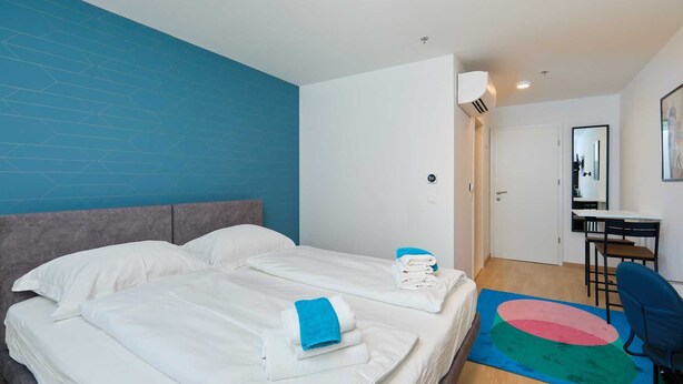 A hotel room with two beds, a desk, a chair, and a colorful rug.