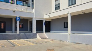 En parkeringsplats med markerade parkeringsrutor, en skylt som visar att platsen är tillgänglig för rullstolsburna och en byggnadsingång med trappsteg.