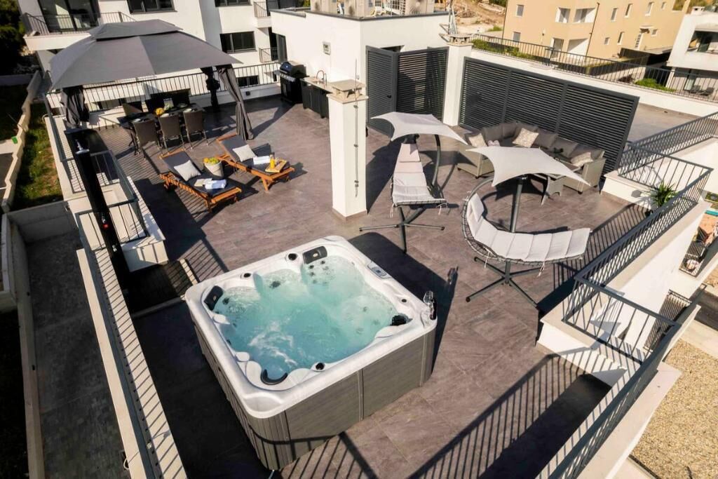 En tagterrasse med jacuzzi, udendørs møbler og en overdækket sektion.