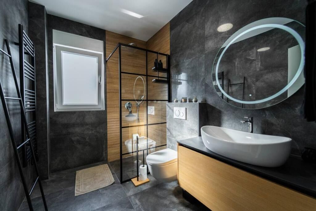 A modern bathroom with a large sink, a round mirror, and a toilet.