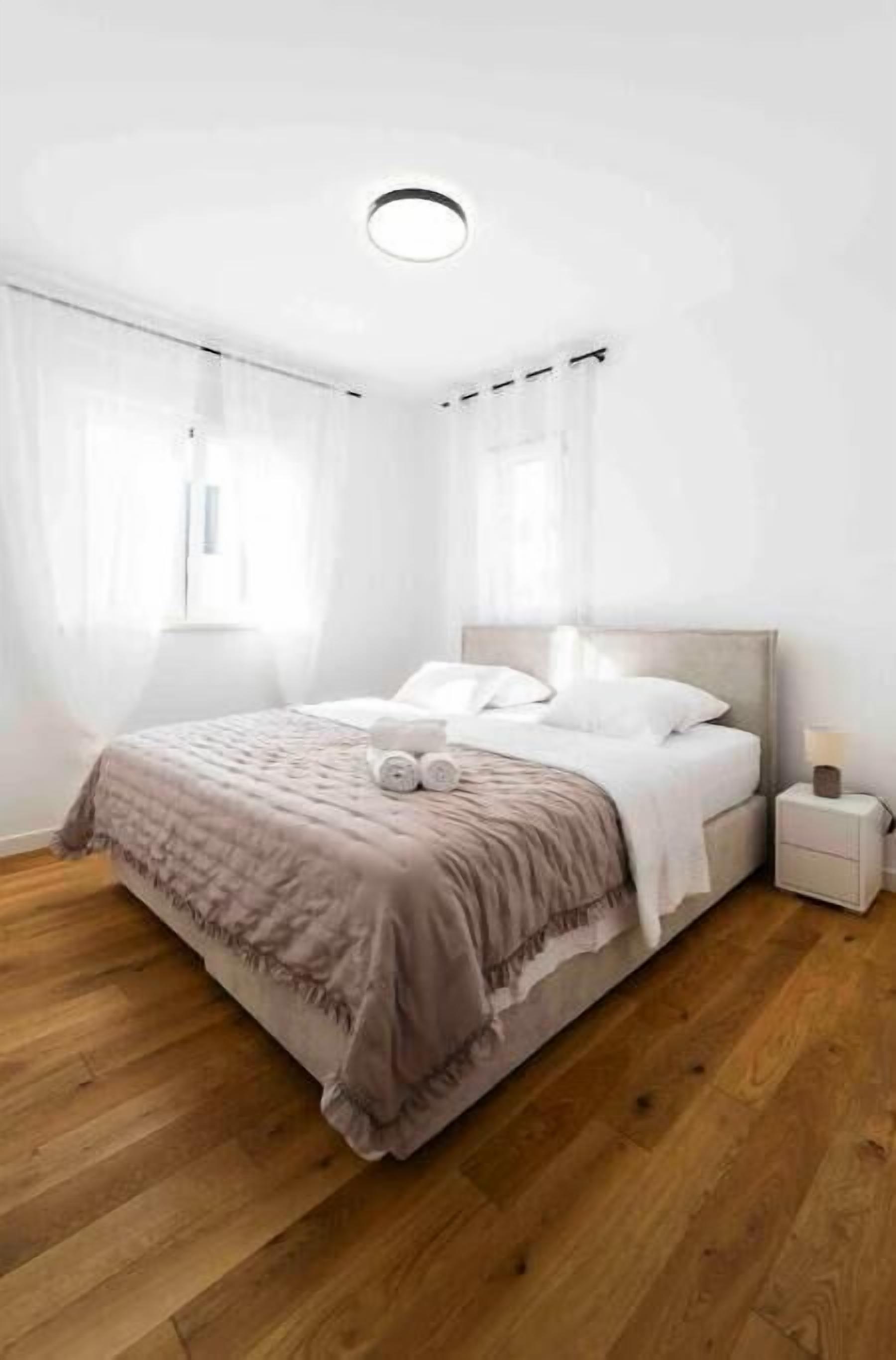 A bedroom with a bed, a nightstand, a window with curtains, and a ceiling light.