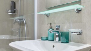 A bathroom with a white sink, a glass shelf above it, and a glass shower enclosure. - R5 Standard double or twin room DOMINIUM CITY SUITES (Dubrovnik)